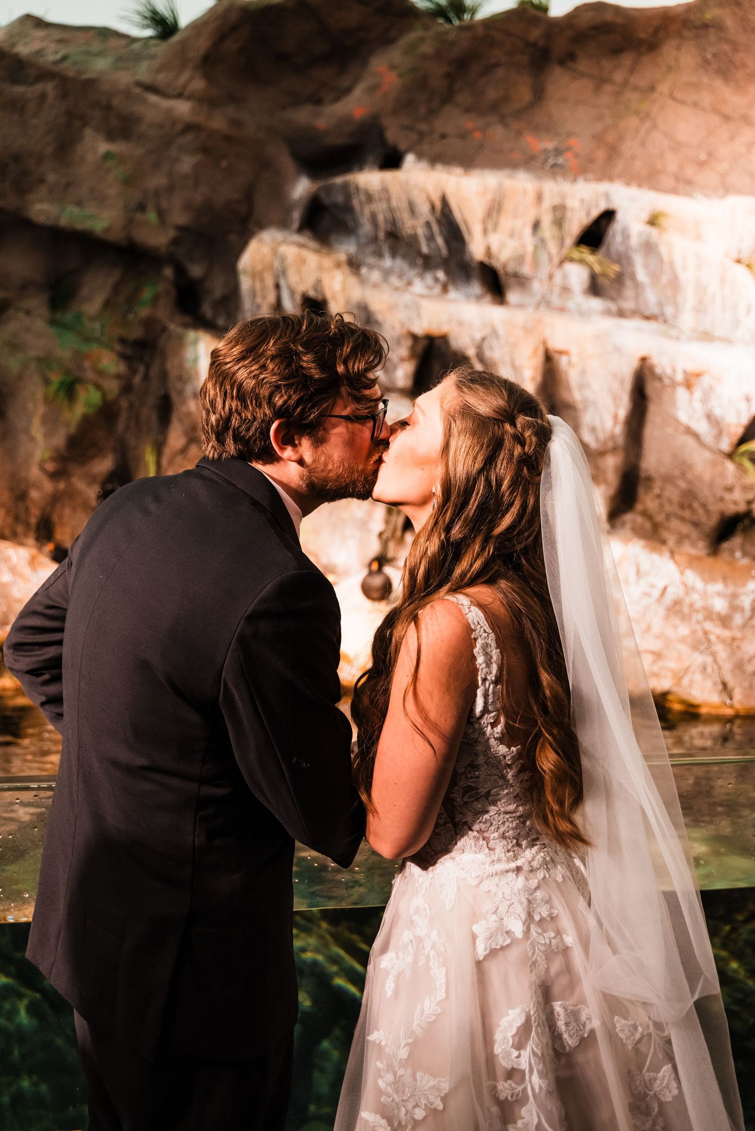 Romantic kiss shared near a waterfall during wedding ceremony.