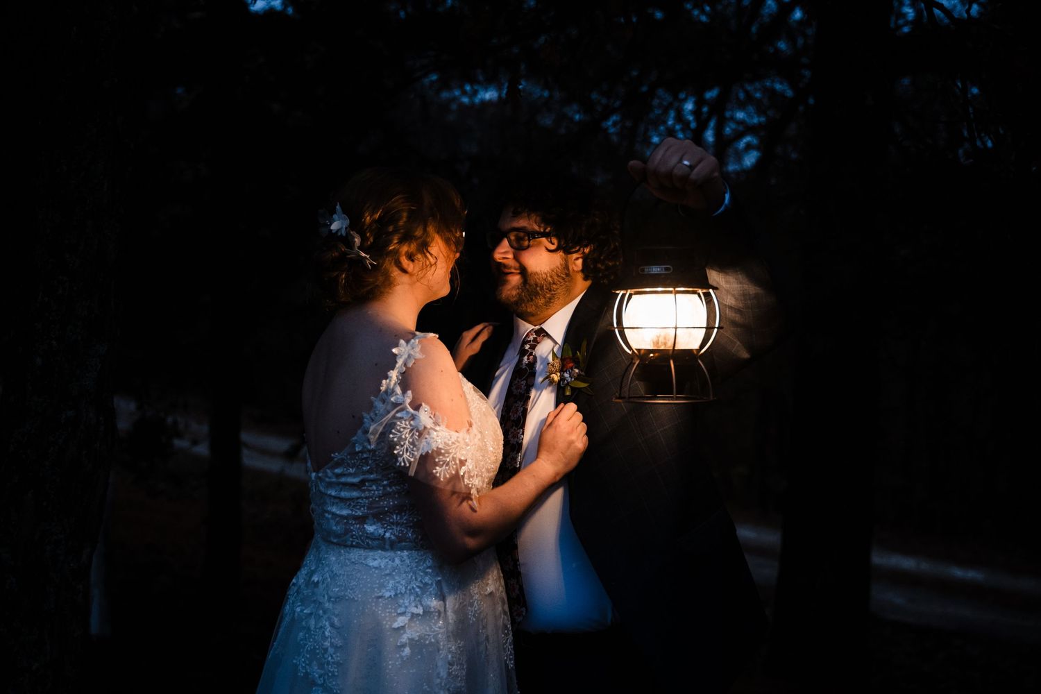 Wedding couple share intimate moment under lantern light at dusk.