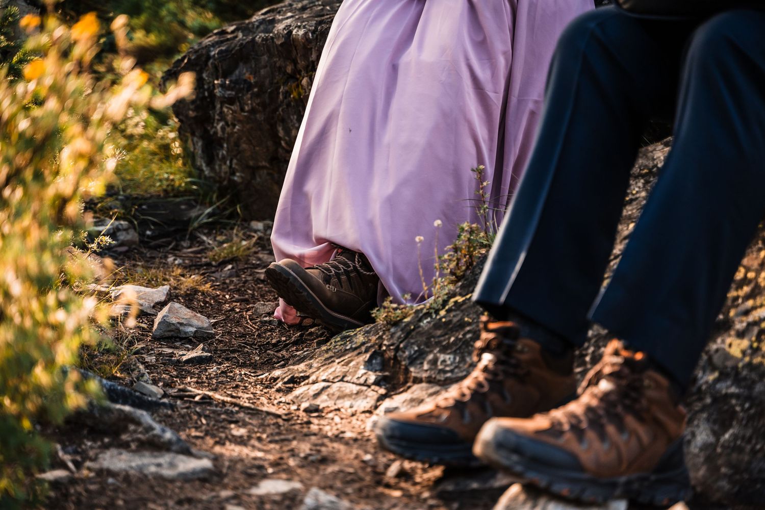 Close-up of hiking boots and flowy dress fabric on a rocky mountain trail.