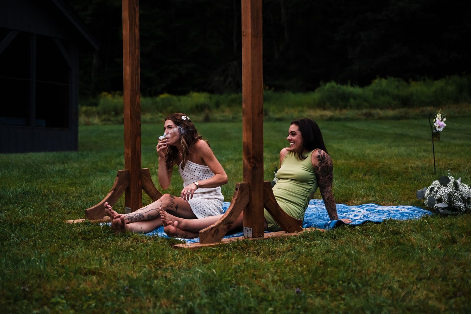 Guests relax on blankets under wooden posts during an outdoor wedding gathering.