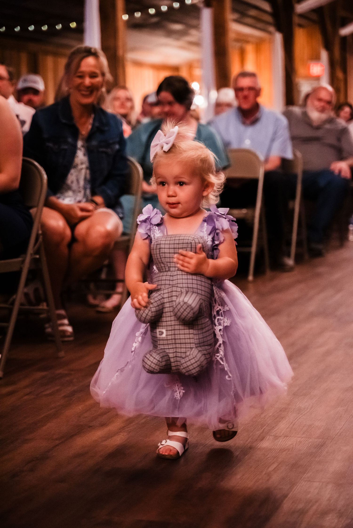 A toddler in a purple tulle dress skips across a wooden dance floor during a wedding reception.