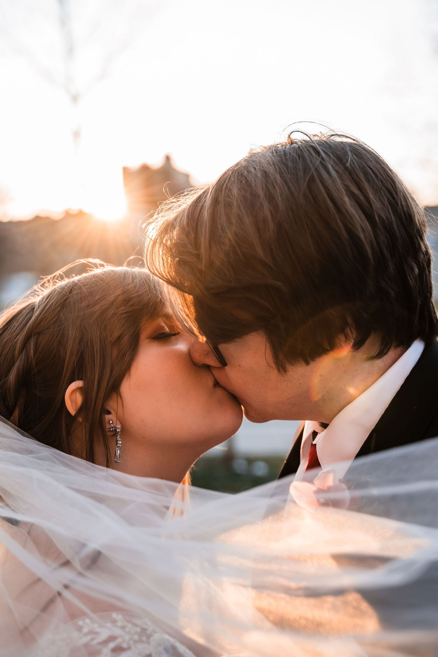 Sunset kiss captured through flowing wedding veil creating romantic silhouette.