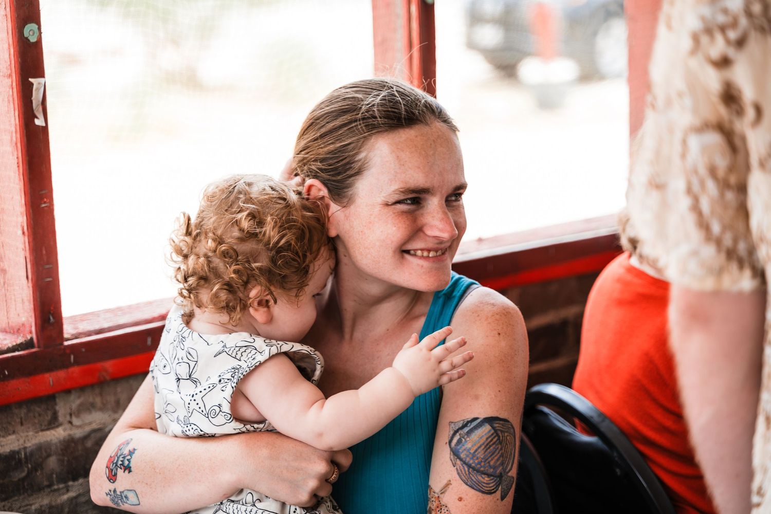 Parent and toddler share a joyful moment together while riding in a red-colored train car or carriage.