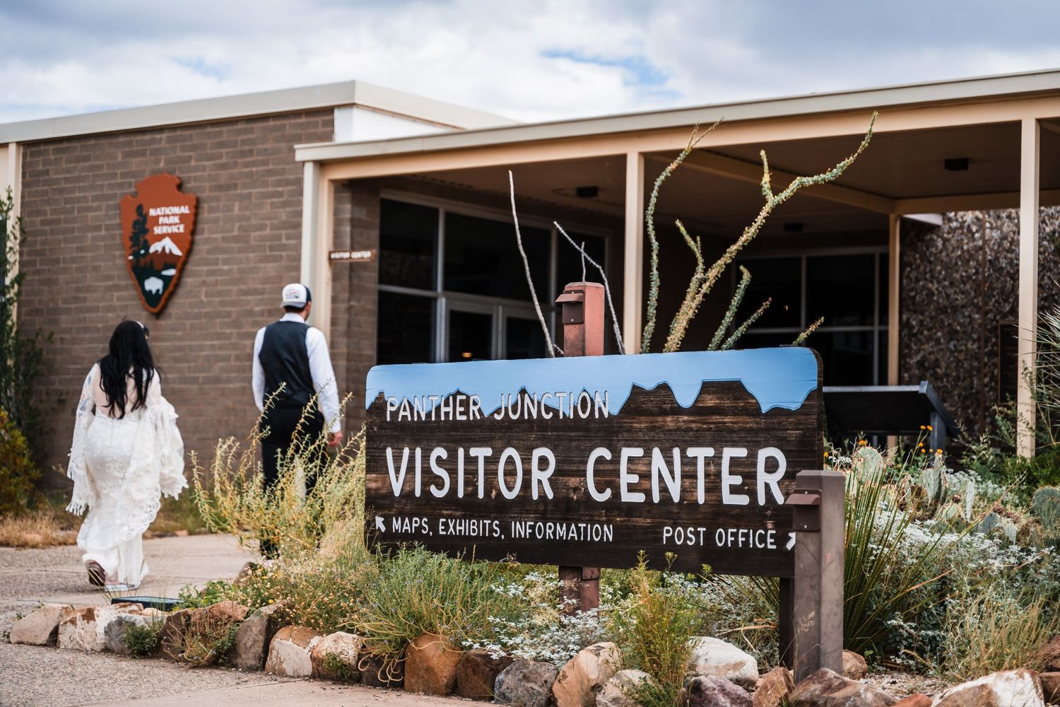 A visitor center entrance sign with desert landscaping and National Park Service logo.