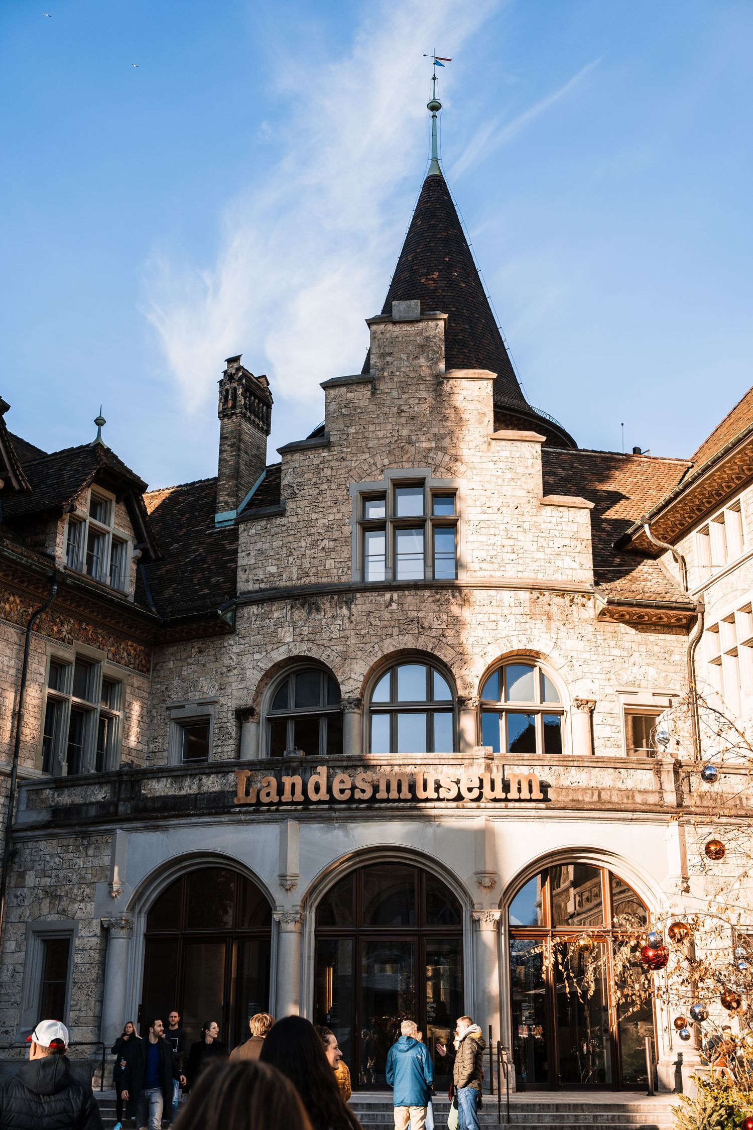 Historic stone facade of the Landesmuseum building with gothic architecture and arched entryways in warm sunlight.