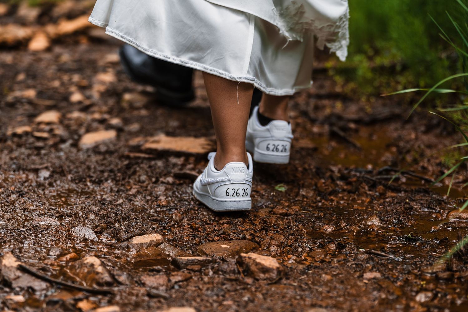 Close-up of bride's custom wedding sneakers with date inscription walking on a muddy mountain trail.