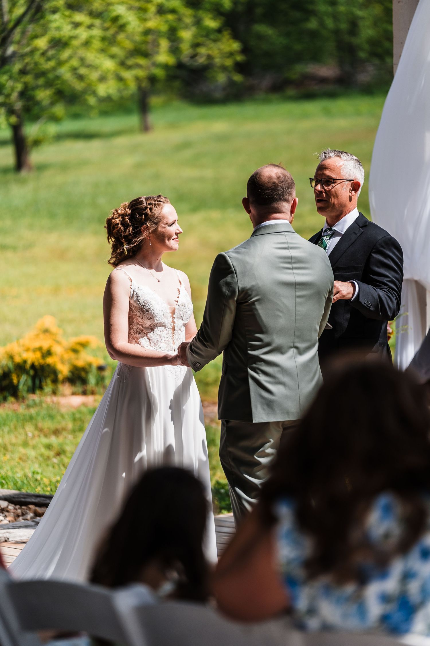 Bride and groom exchange vows outdoors with officiant in lush green garden wedding ceremony.