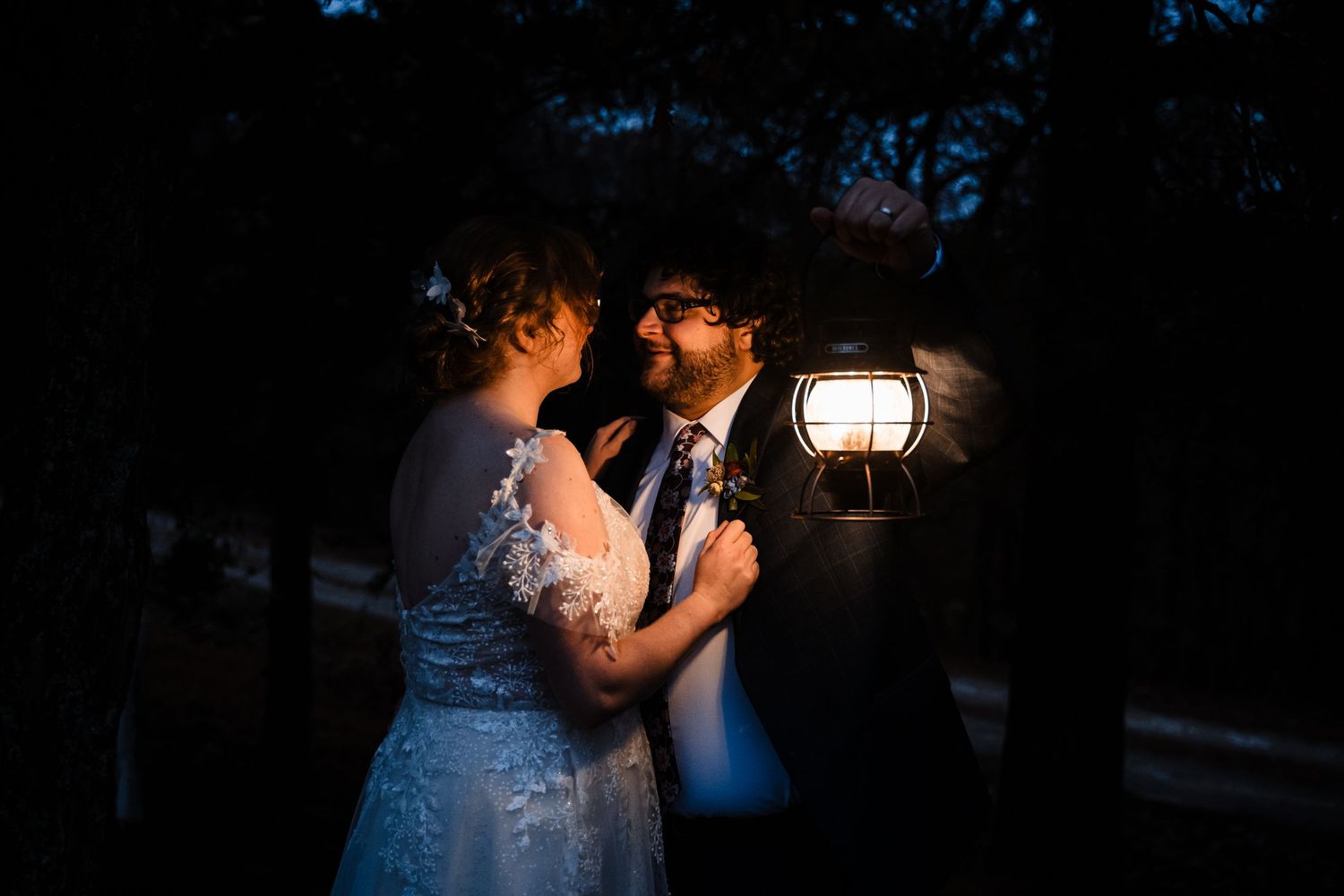 A romantic evening wedding moment illuminated by a soft lantern glow in a dark outdoor setting.