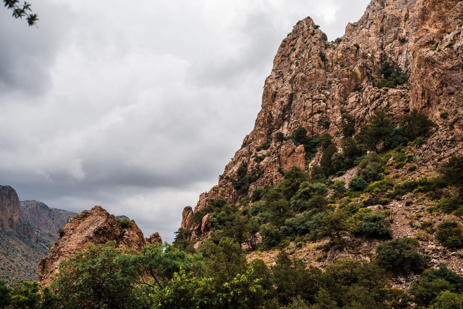 Dramatic rocky mountain peaks under cloudy skies in a desert landscape.