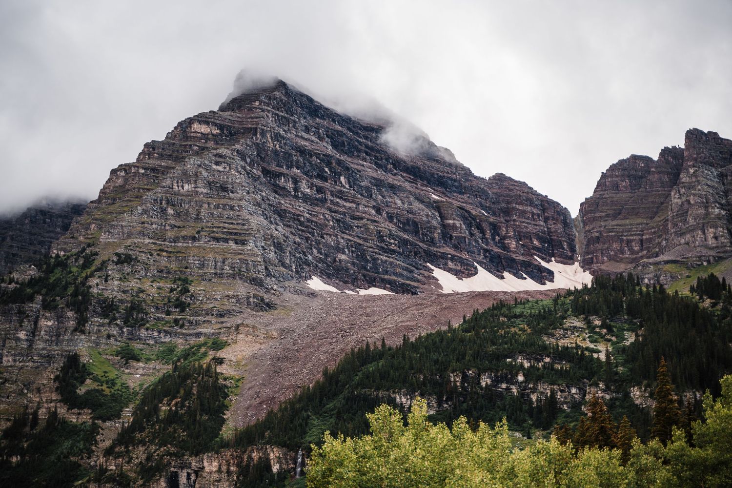 Dramatic rocky mountain peak with traces of snow and low-hanging clouds in a moody landscape setting.