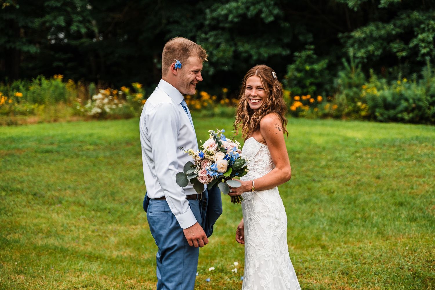 A couple shares a candid moment during their outdoor wedding photoshoot in a garden setting.