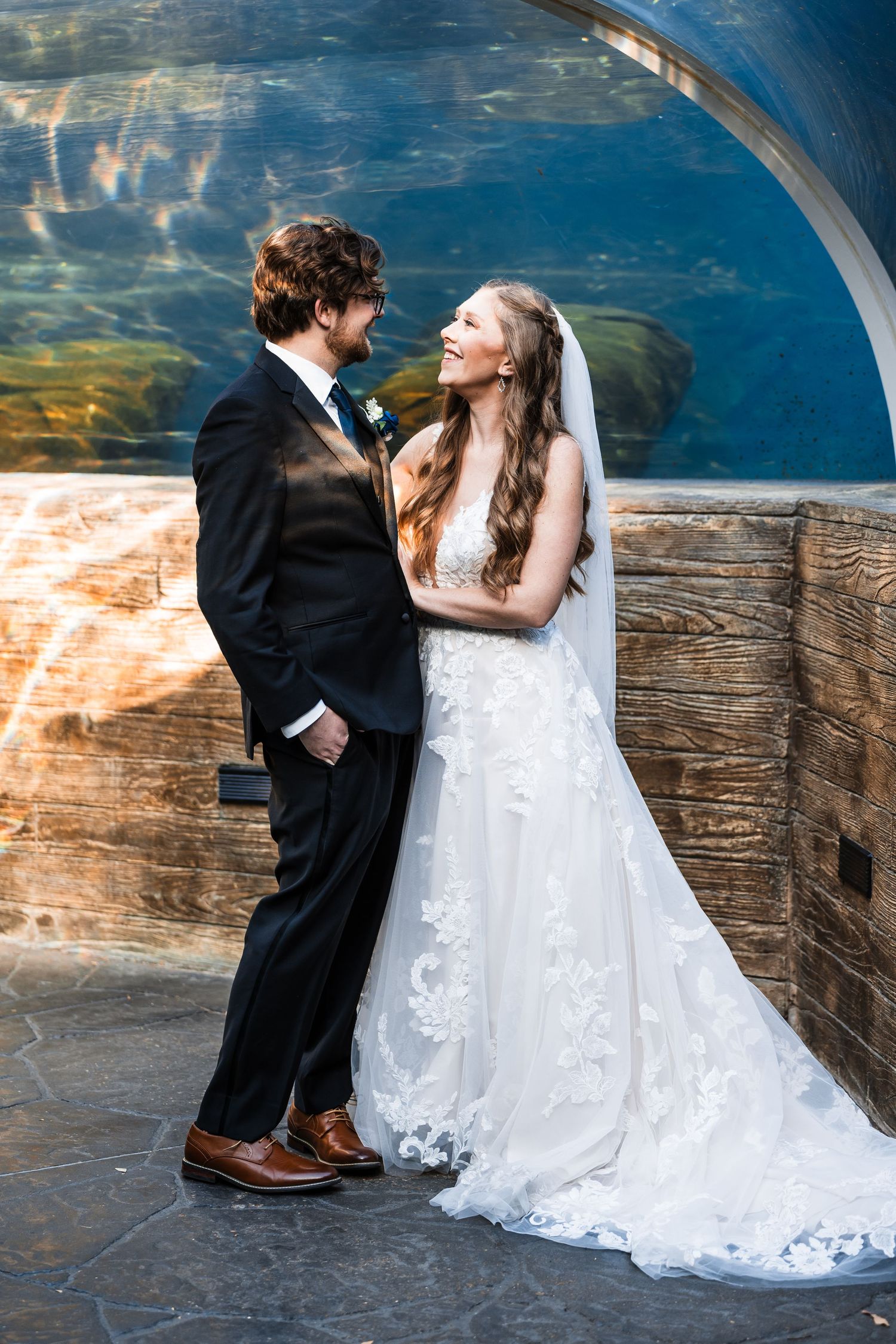 Bride and groom share romantic moment against curved aquarium wall background.