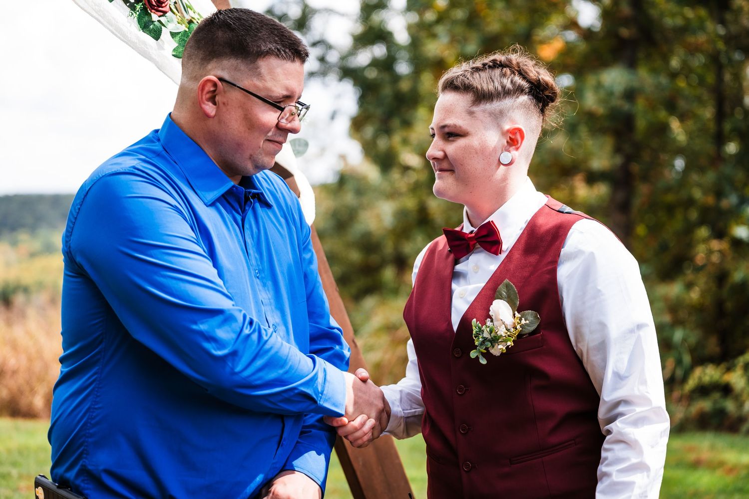 A heartfelt handshake between two formally dressed people at an outdoor wedding celebration.