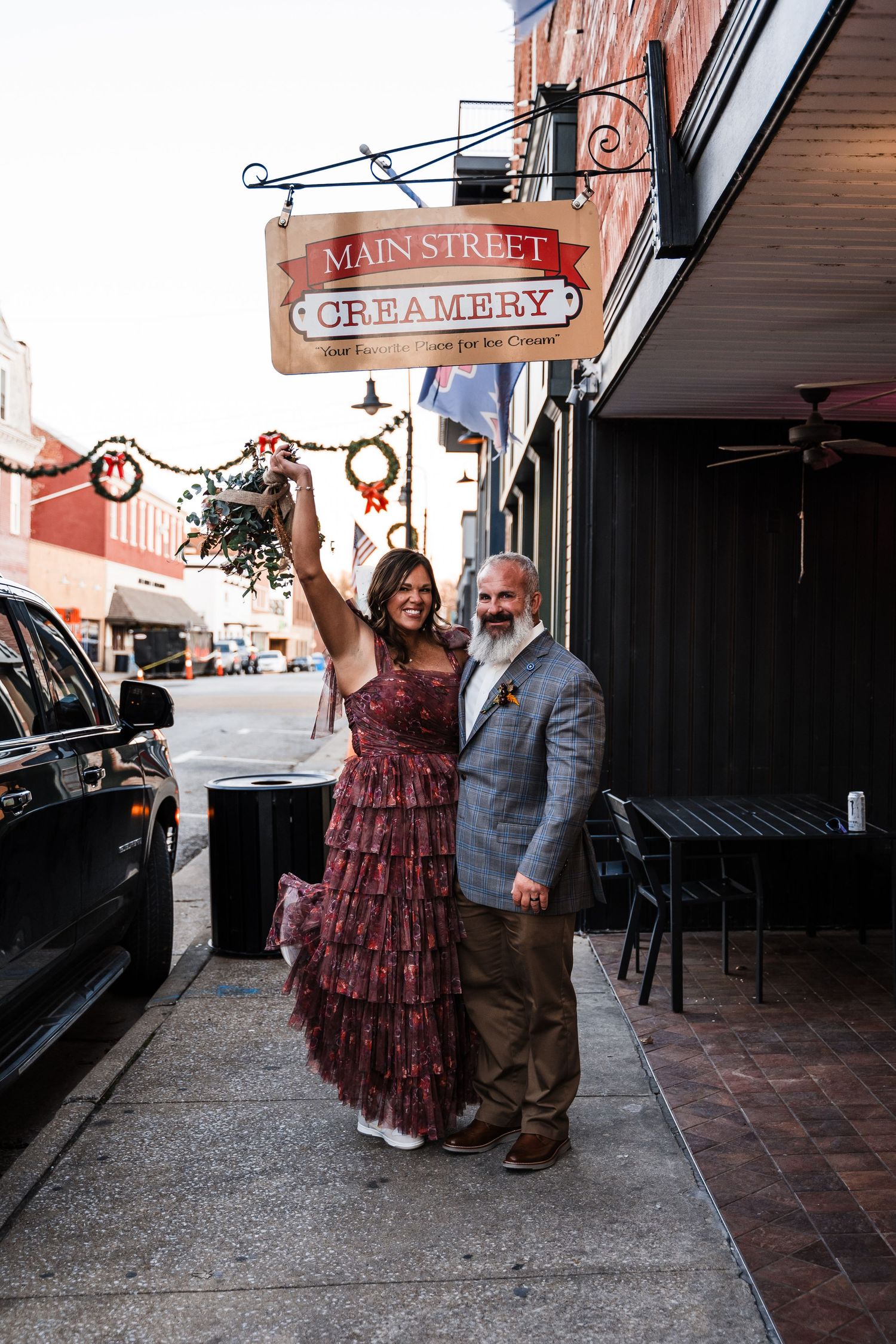 A couple poses excitedly outside Main Street Creamery beneath a vintage storefront sign.
