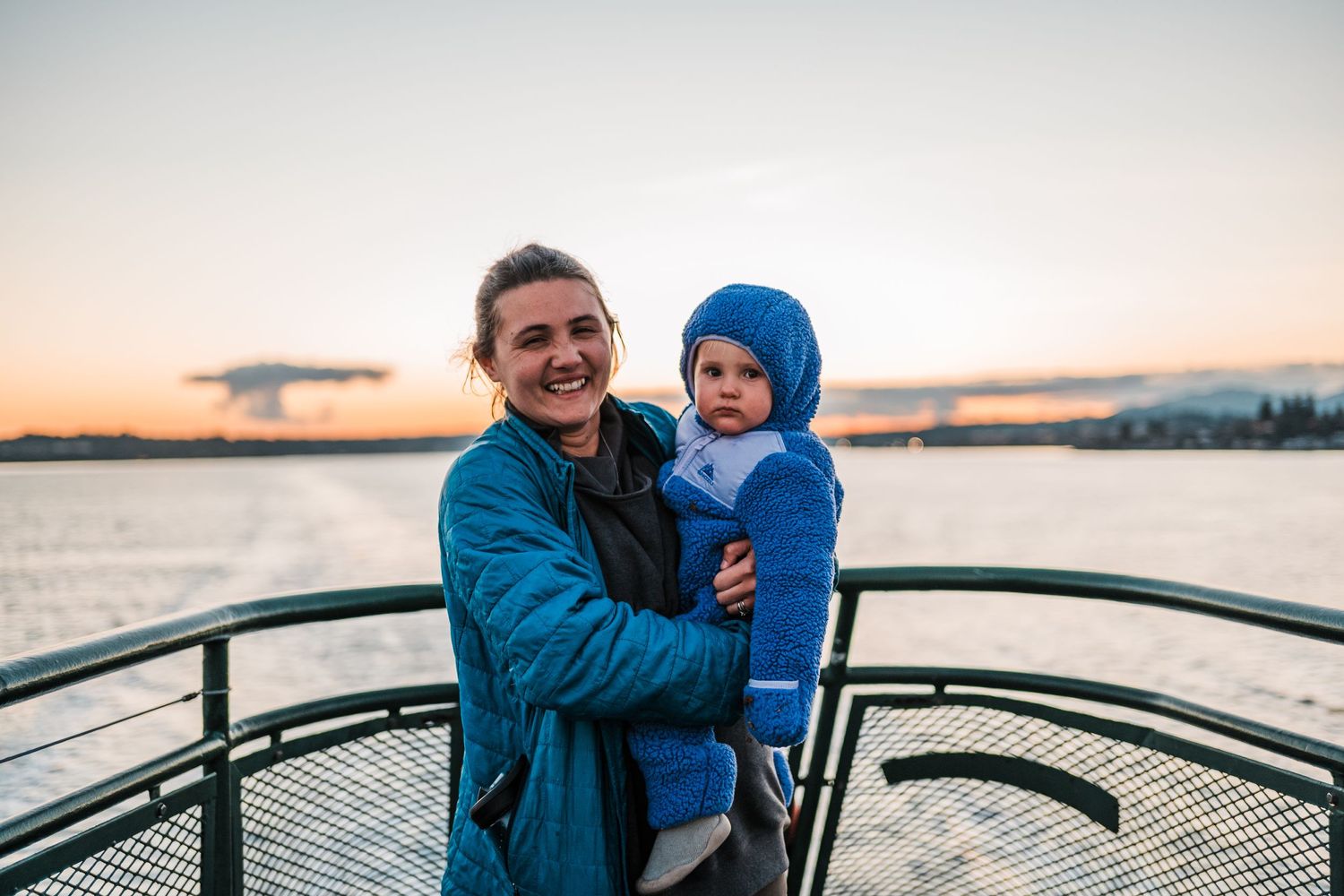 A cheerful scene on a ferry deck against a sunset sky and water view.