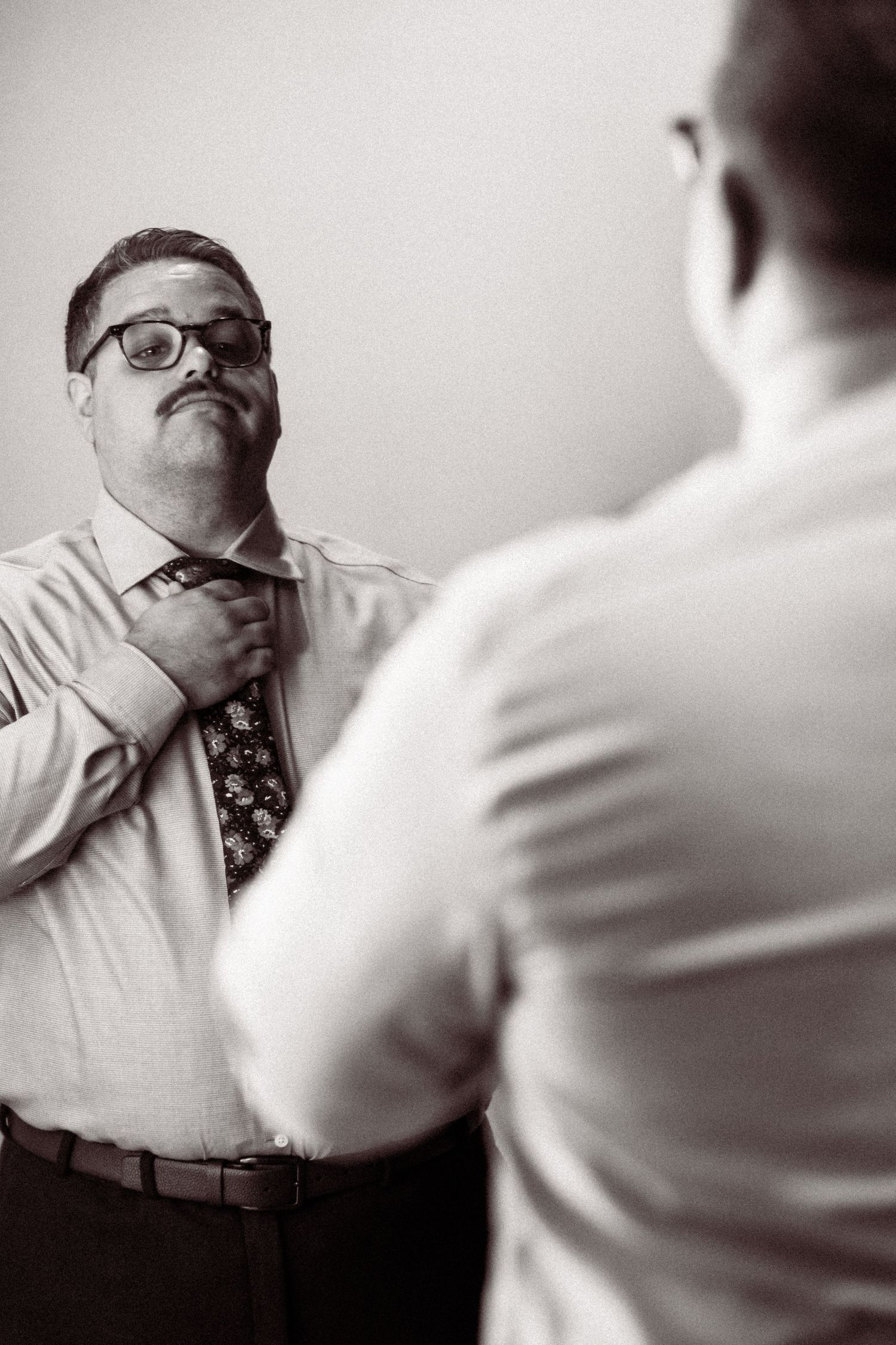 A series of black and white photos showing someone in glasses and a tie gesturing with their hand over their face.