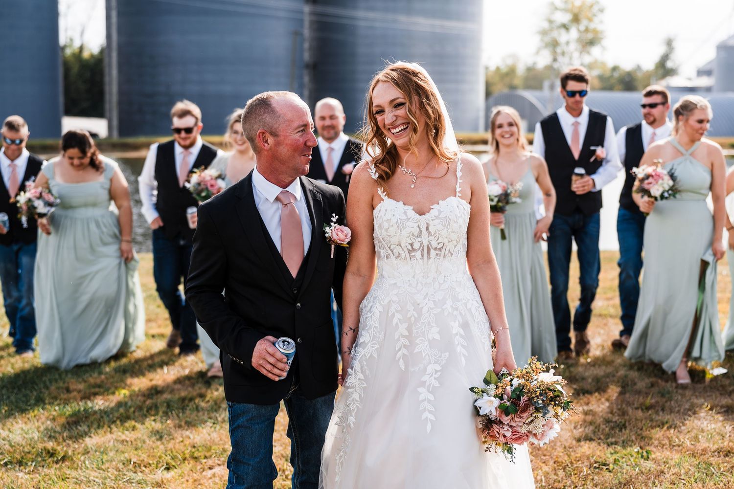 A joyful outdoor wedding scene with wedding party members in sage green dresses watching the couple.