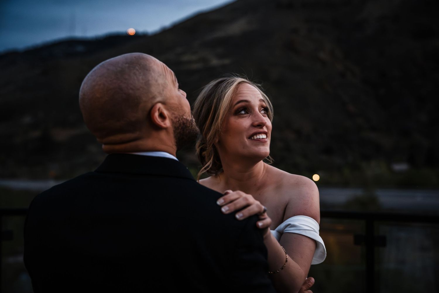 Bride gazes lovingly at groom during romantic first dance at dusk mountain wedding.
