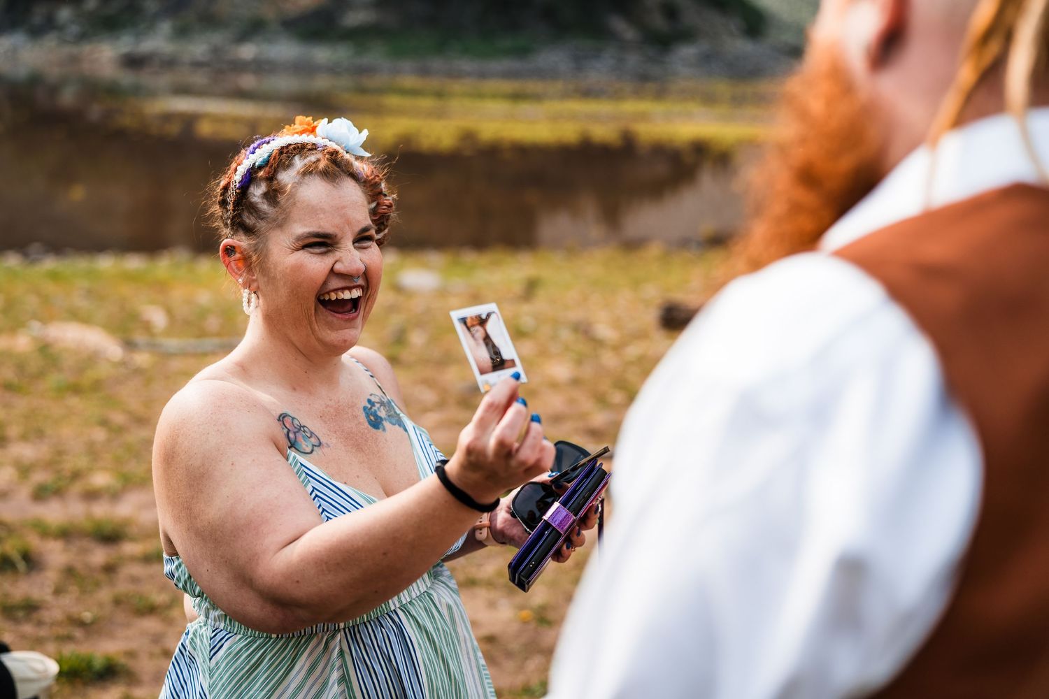 Laughing bride shows tarot card to redheaded groom during outdoor mountain wedding ceremony.