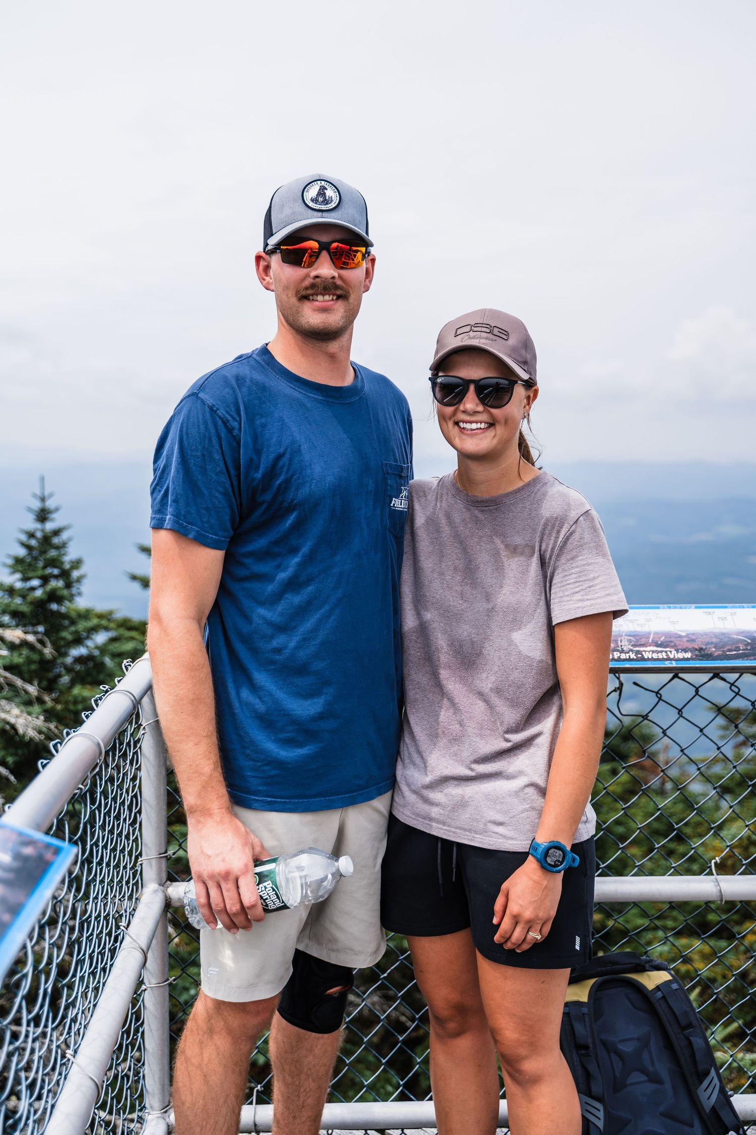 Outdoor enthusiasts pose together on a scenic mountain overlook with safety railing.