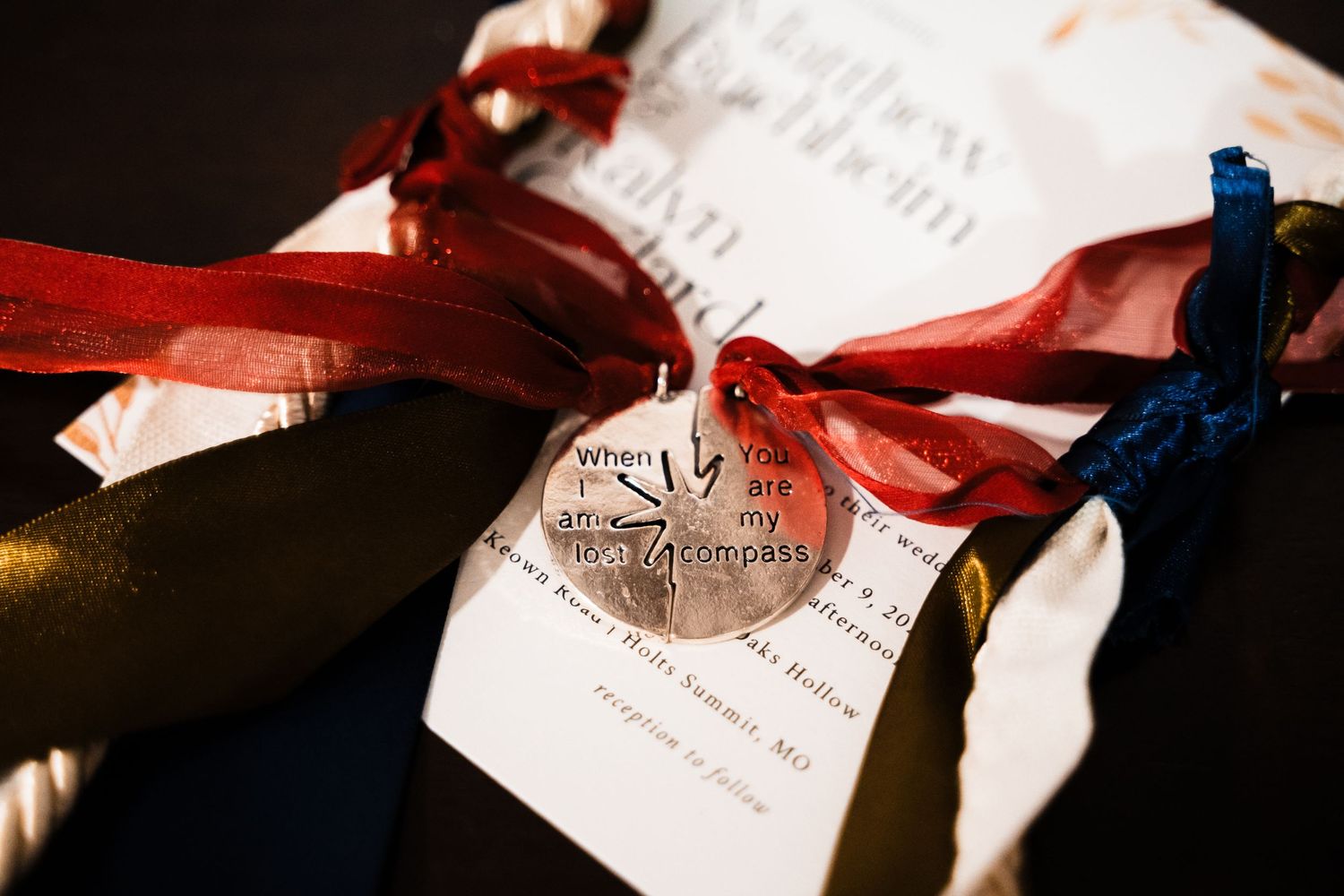 Close-up of wedding invitation with red and blue ribbons and decorative charm.