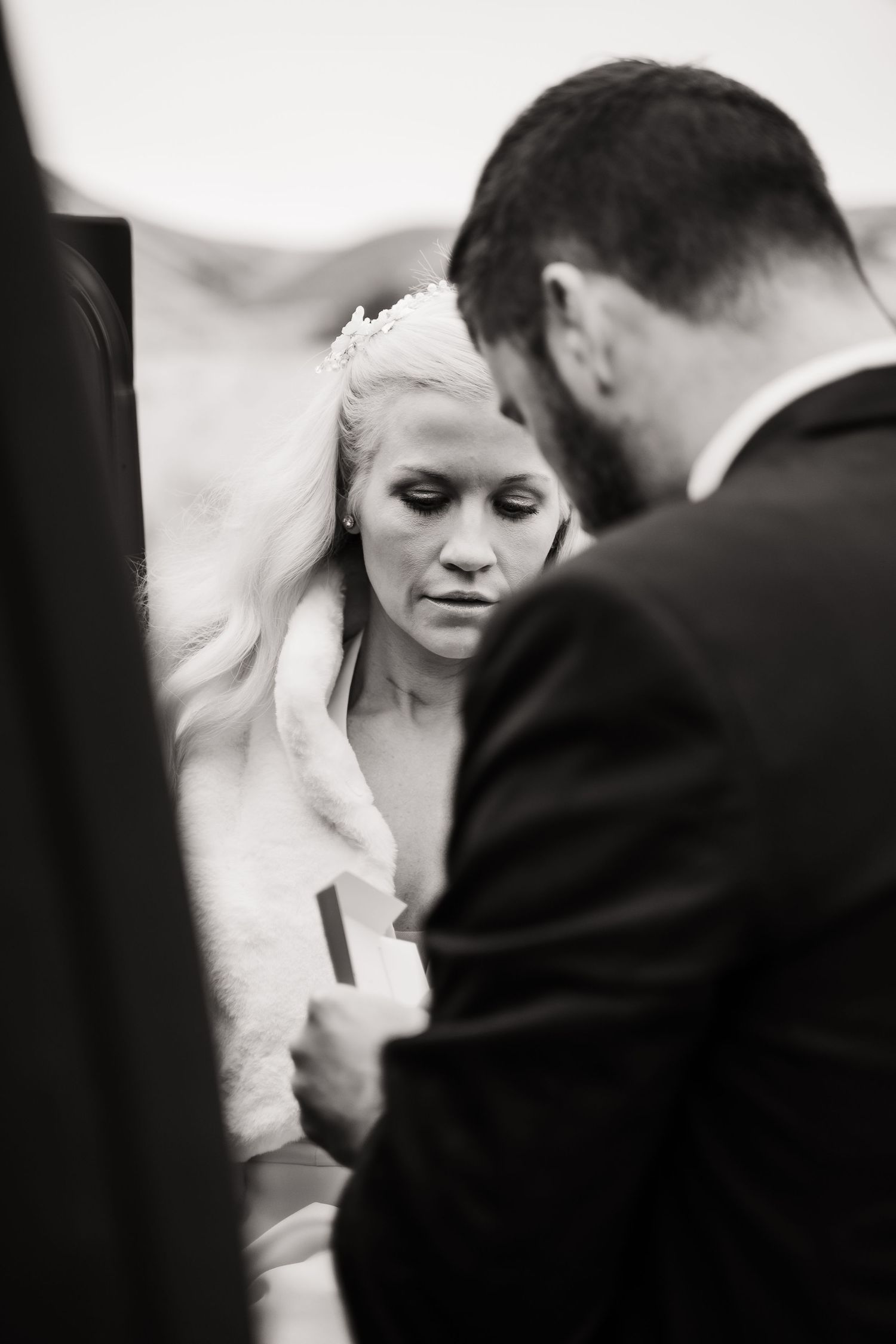 An intimate black and white wedding moment captured near a vehicle.