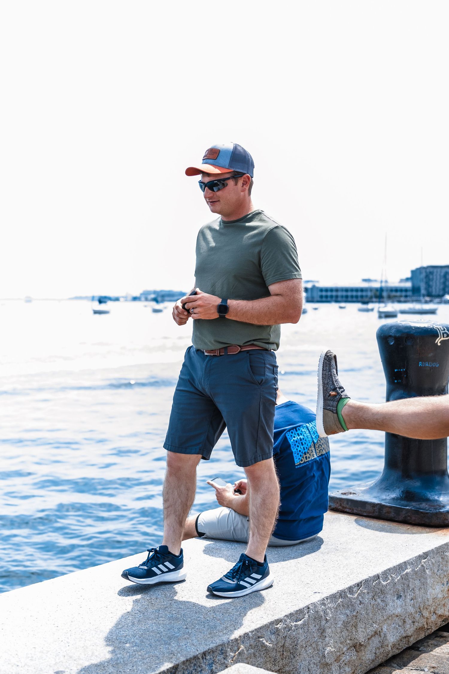 Person in casual attire standing on waterfront pier with blue ocean in background.