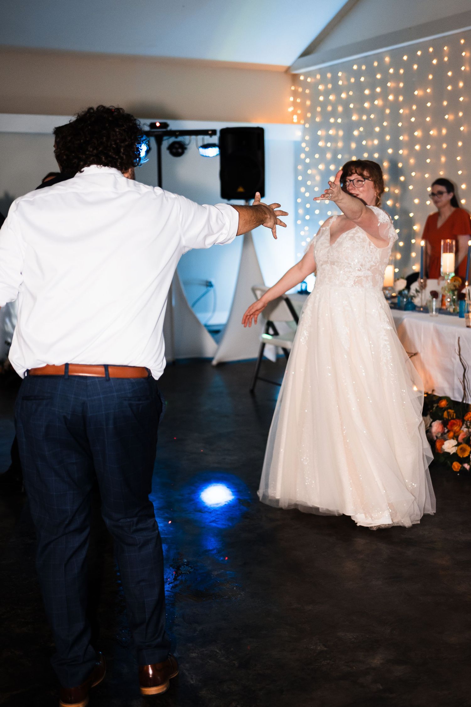 A couple shares a dance moment on the reception floor with string lights in the background.