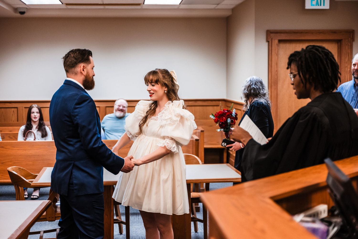 A wedding ceremony taking place in a courthouse room with wood paneled walls.