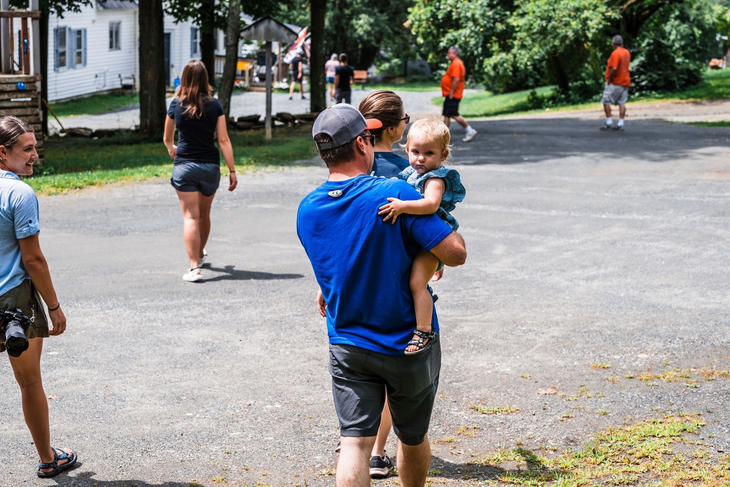 People enjoying a summer day at a park with trees and paved paths in the background.