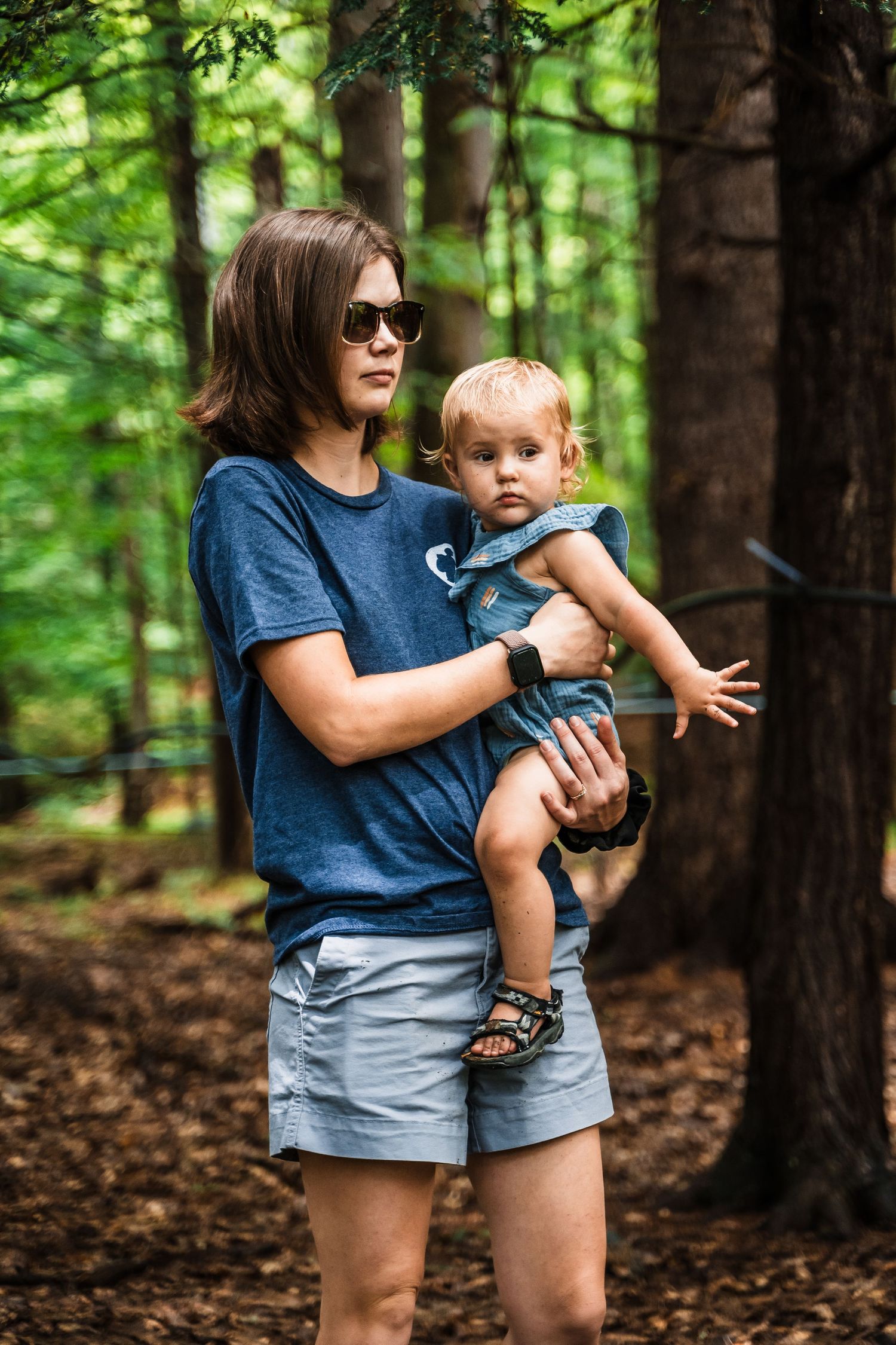 An adult and toddler explore a lush forest trail together on a summer day.
