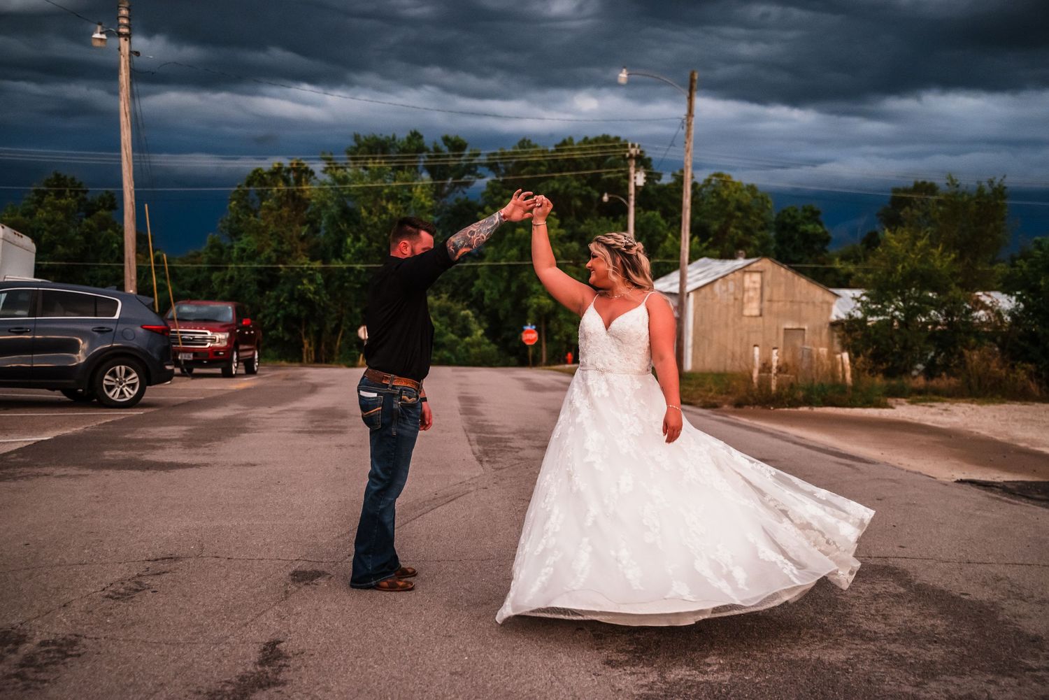 Couple dancing in a parking lot at sunset with dramatic storm clouds overhead.