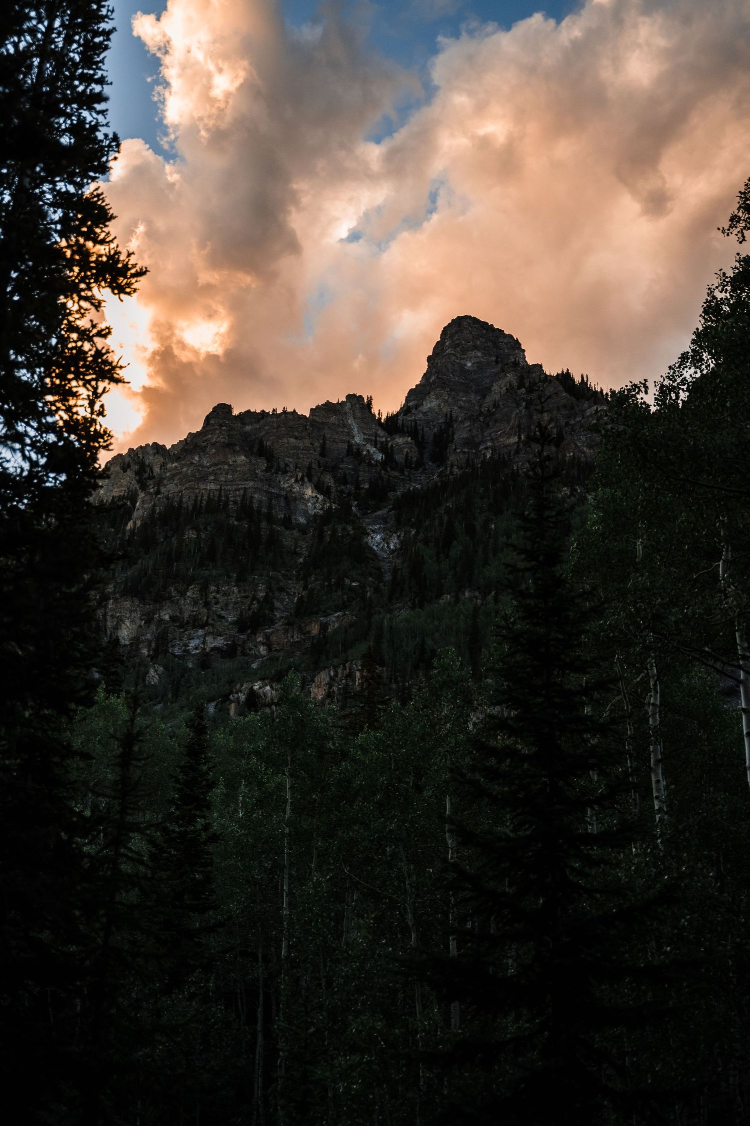 Dramatic orange sunset clouds over mountain peak silhouetted by evergreen trees.