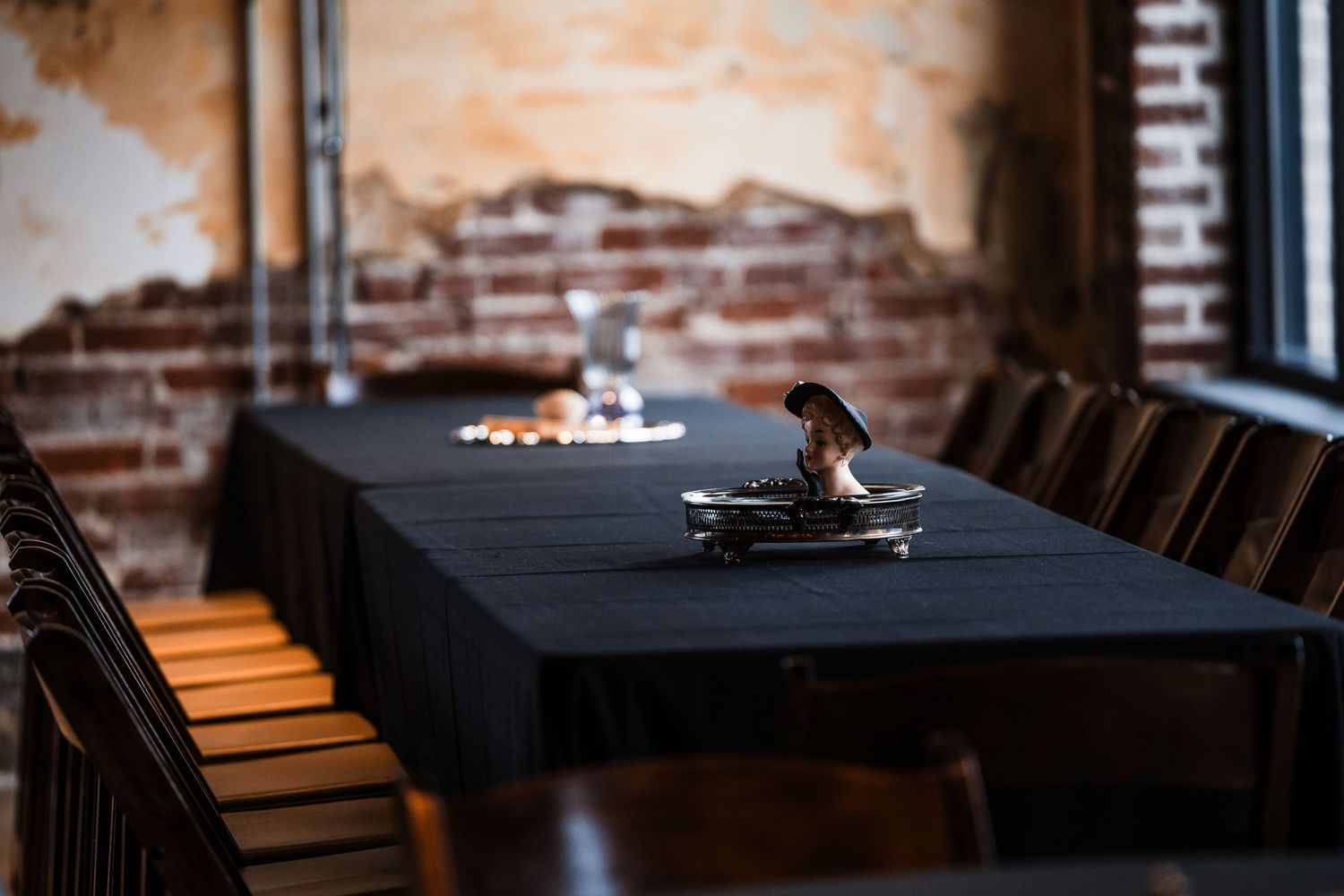 Empty table setting with black tablecloth and chairs in a rustic brick-walled restaurant.