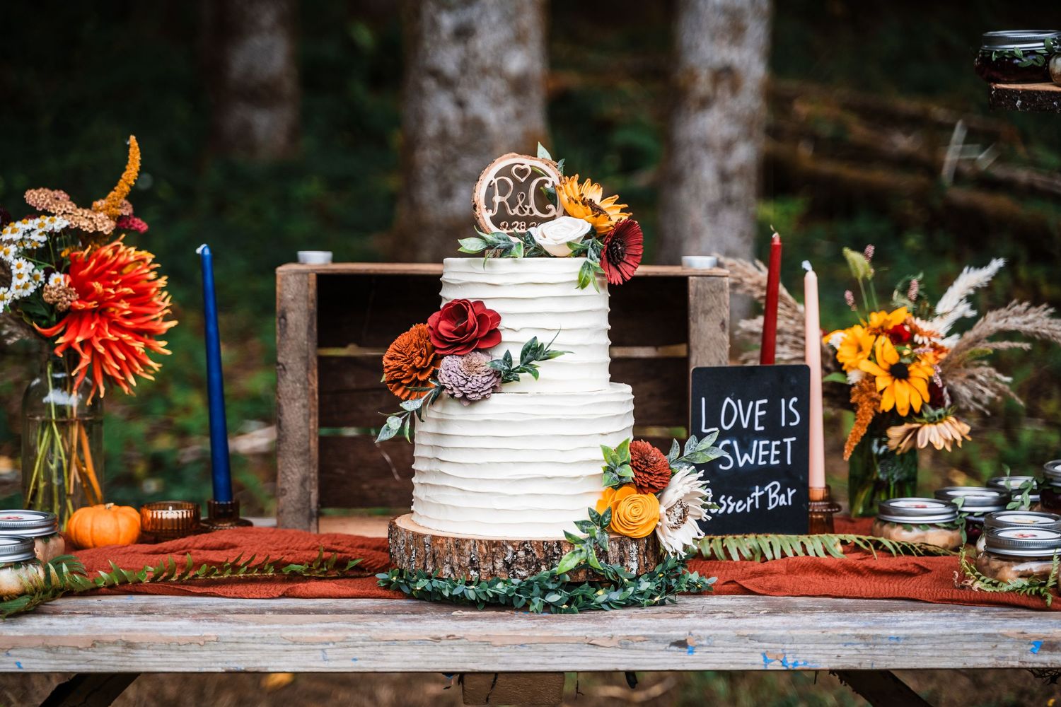 Rustic wedding cake display with sunflowers and autumn decorations on wooden table.
