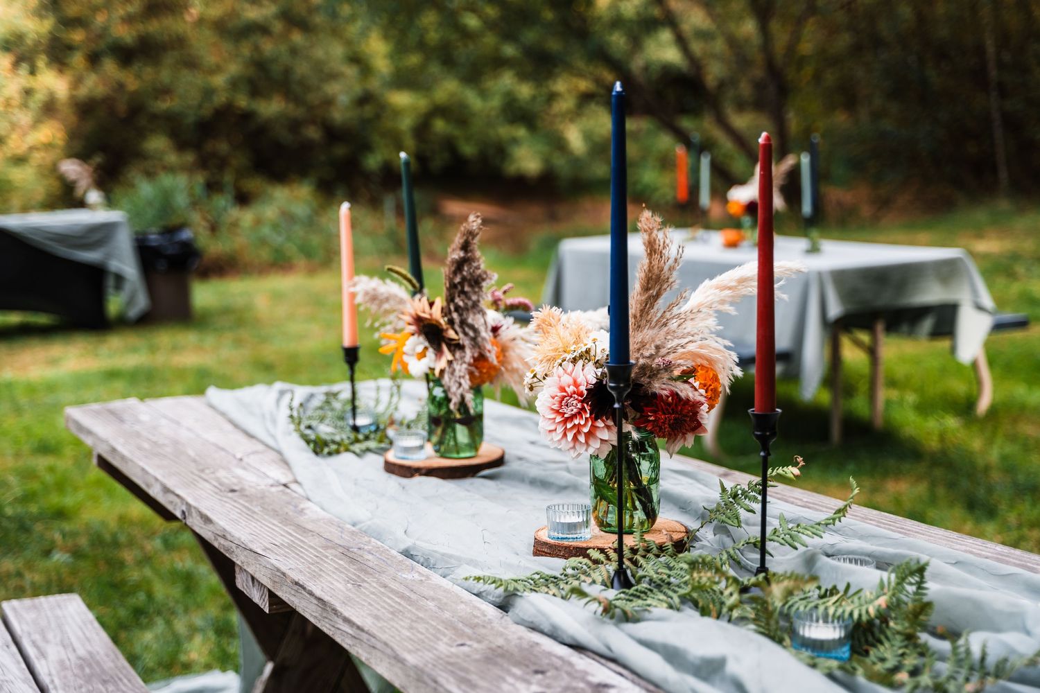 Rustic outdoor table setting with tall candles and floral arrangements on weathered wood for garden dining.
