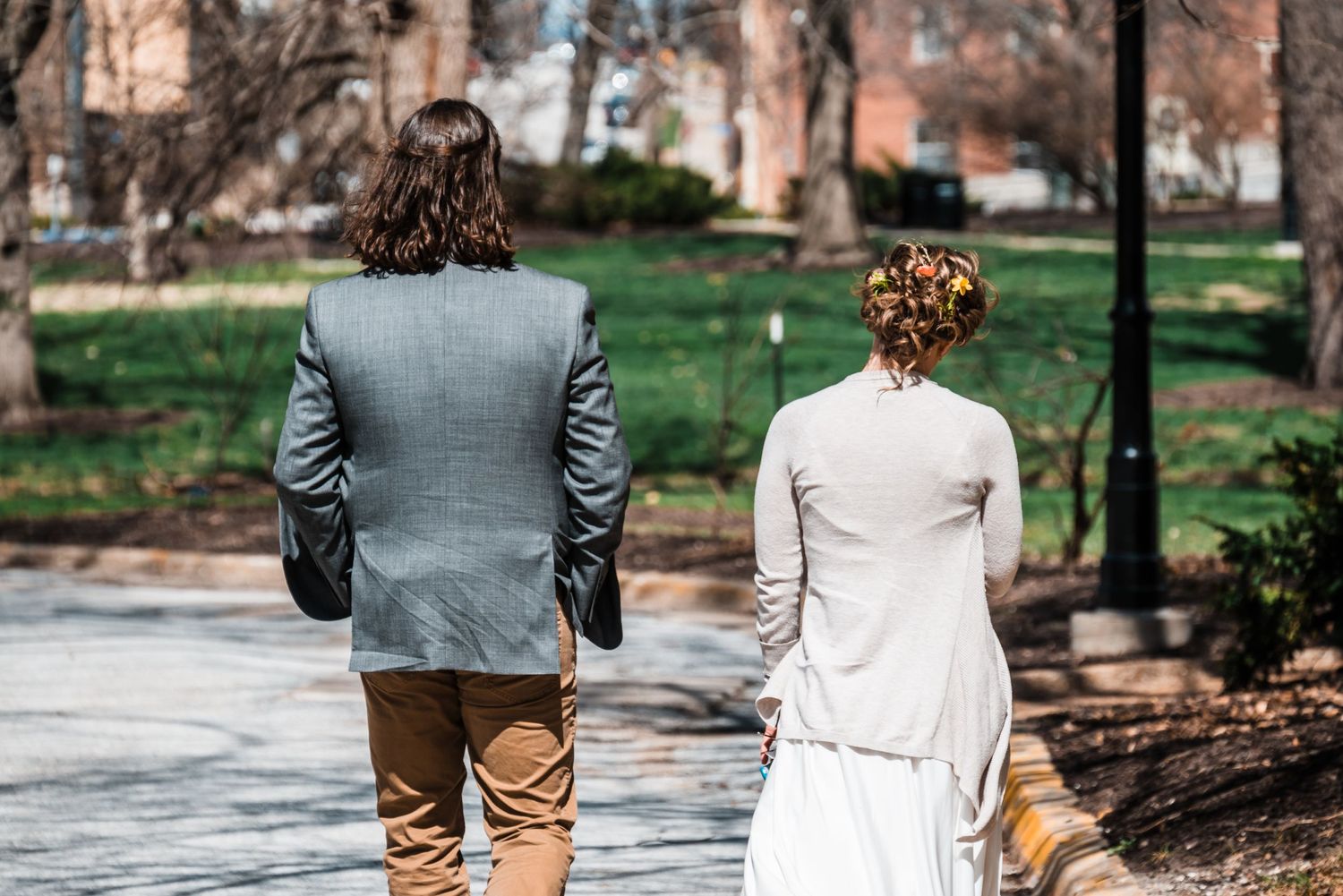 A couple in wedding attire walking down a tree-lined path on a spring day.