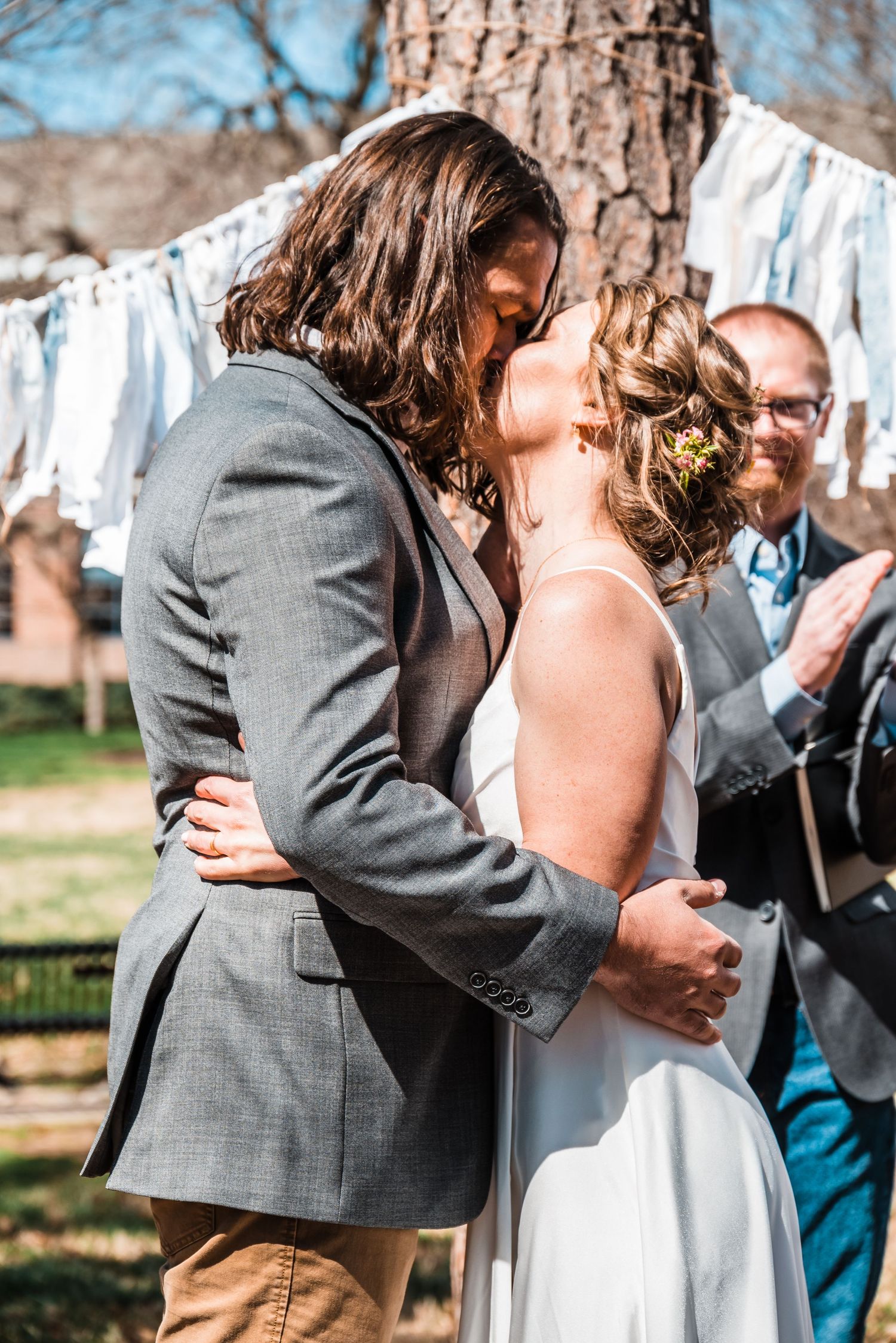 A couple shares an intimate moment during their outdoor wedding ceremony with white banners behind them.
