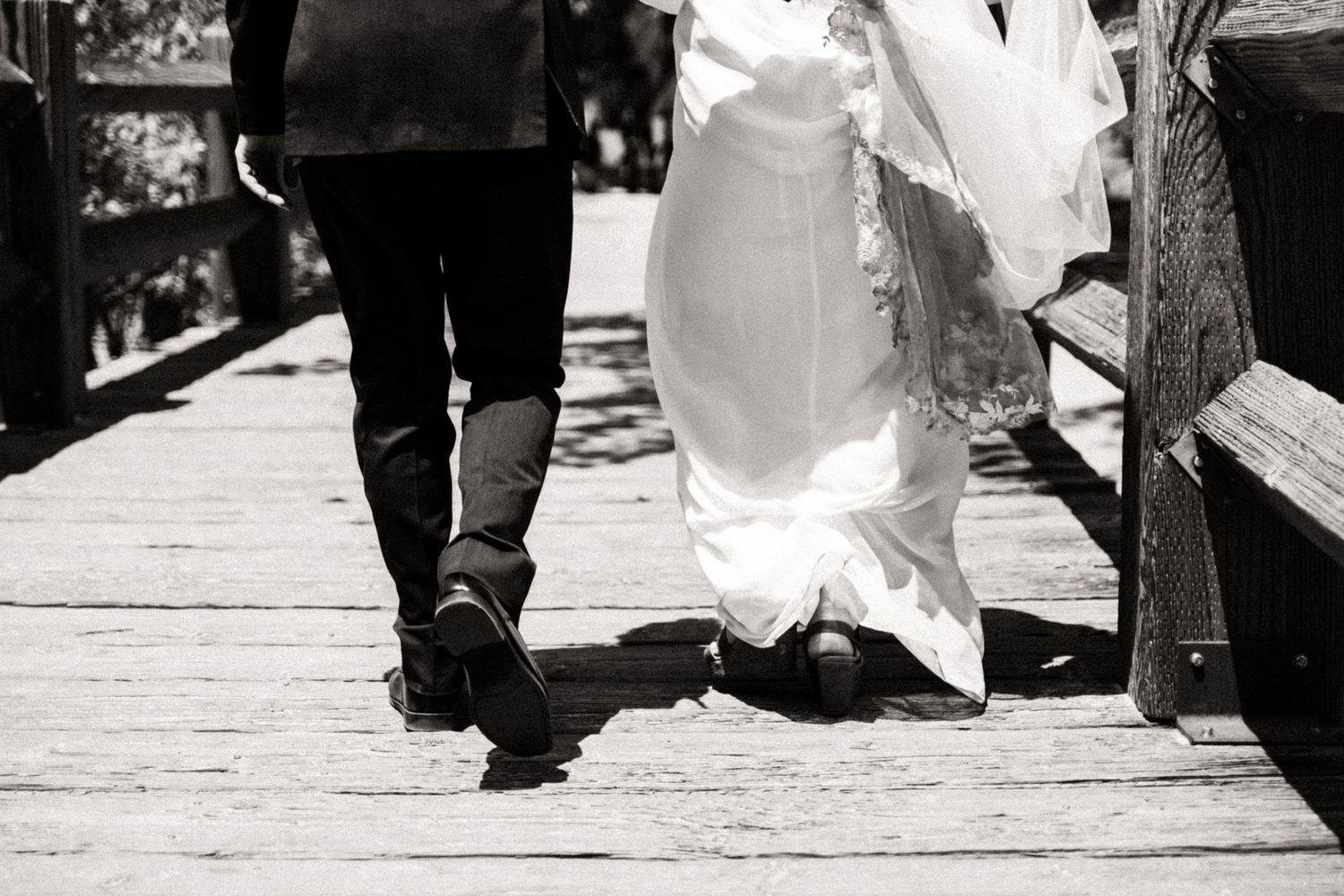 Black and white shot of feet walking on a wooden boardwalk showing one person in boots and another in a white dress.