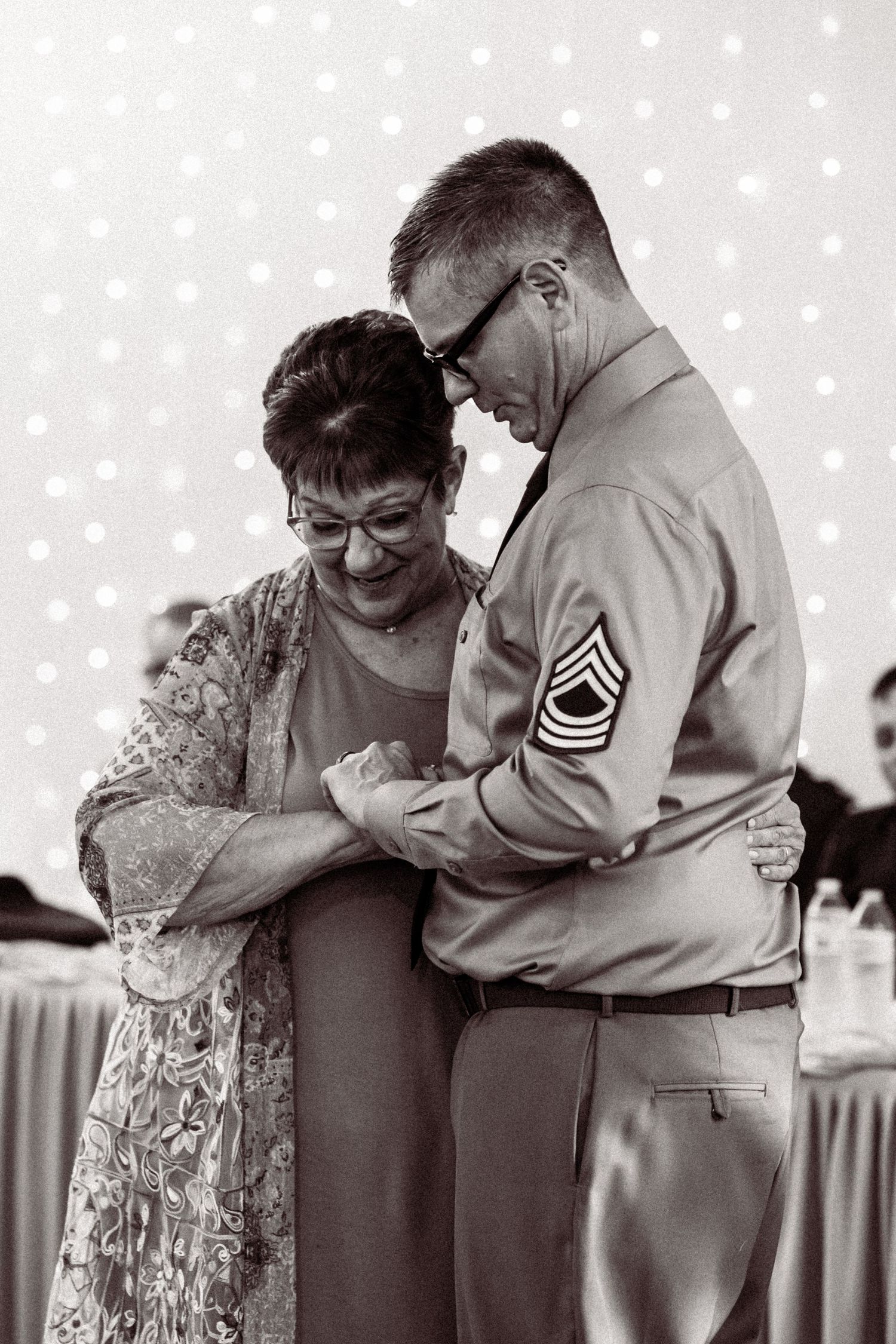 Black and white photo of a couple sharing an intimate dance moment with twinkle lights behind them.