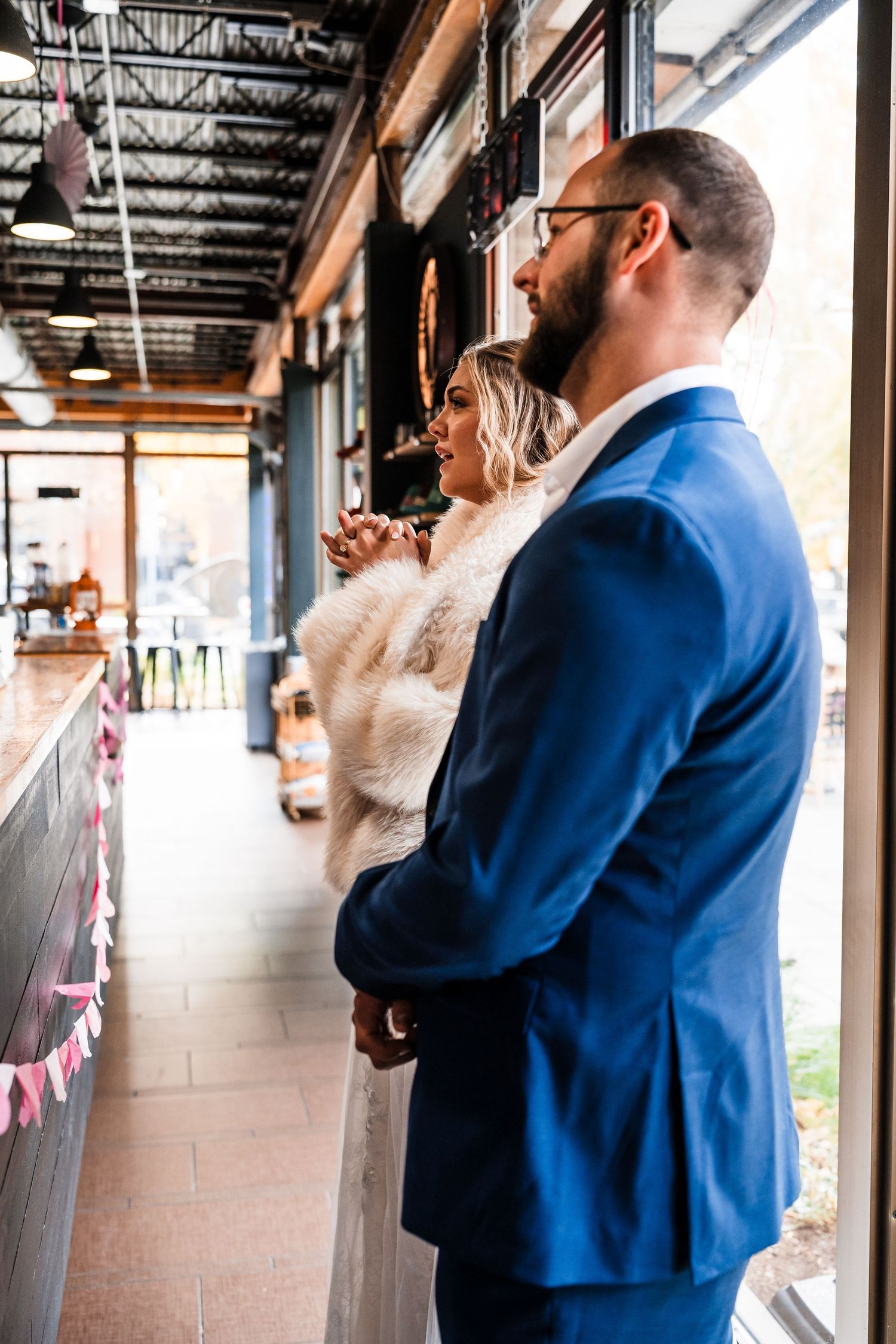 A couple in wedding attire share a private moment in an industrial-style hallway.