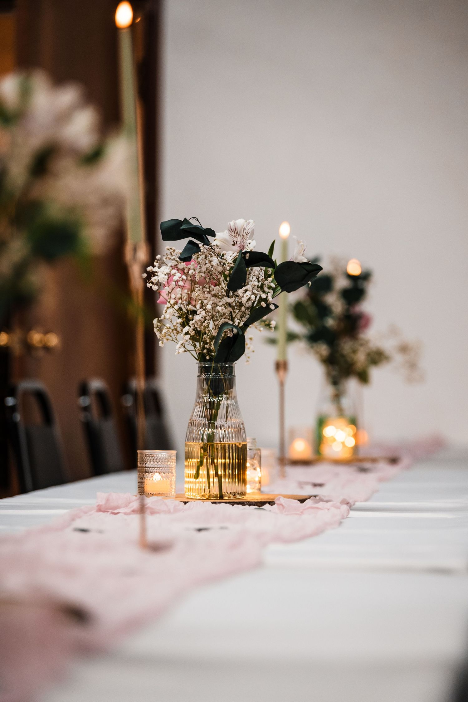 Elegant wedding reception table settings with soft candlelight and delicate floral centerpieces in glass vases.