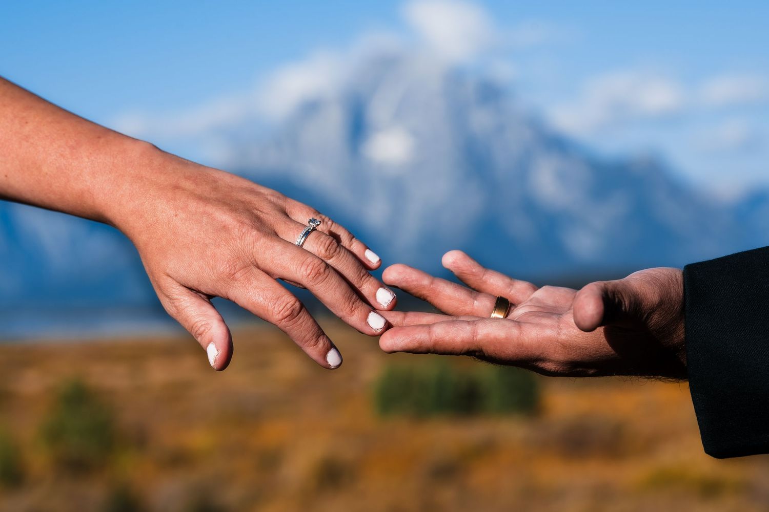 Close-up of wedding rings and hands against mountain backdrop during ceremony.