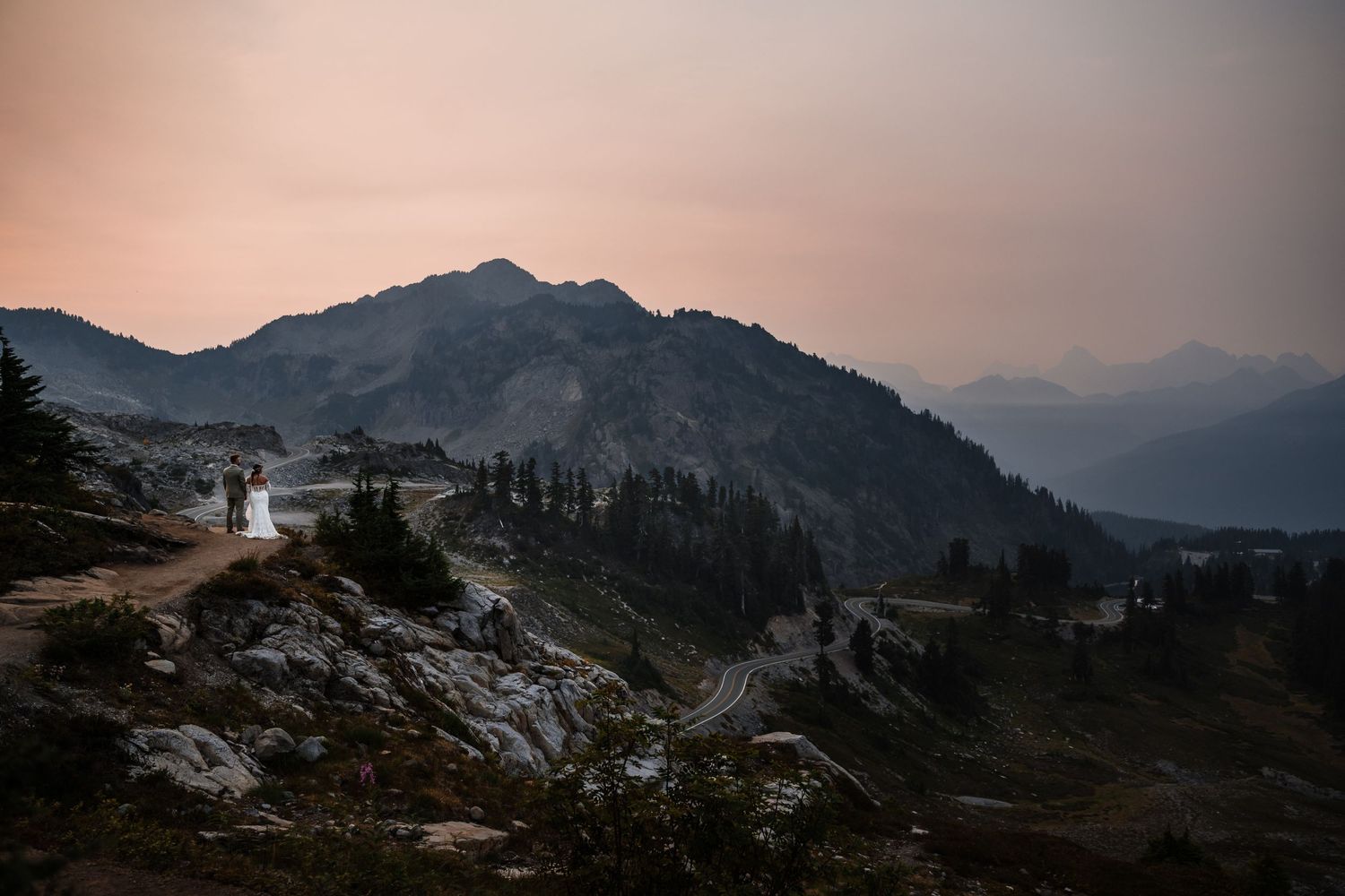 Dramatic mountain landscape at sunset with rocky peaks silhouetted against a dusky pink and purple sky.