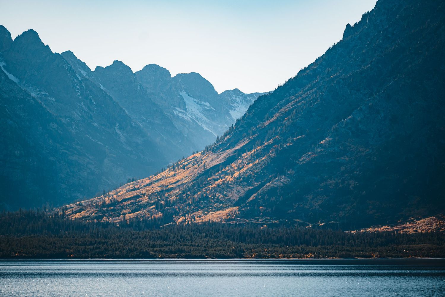 Dramatic panoramic view of rugged mountain peaks and valleys illuminated by golden sunlight against a moody sky.