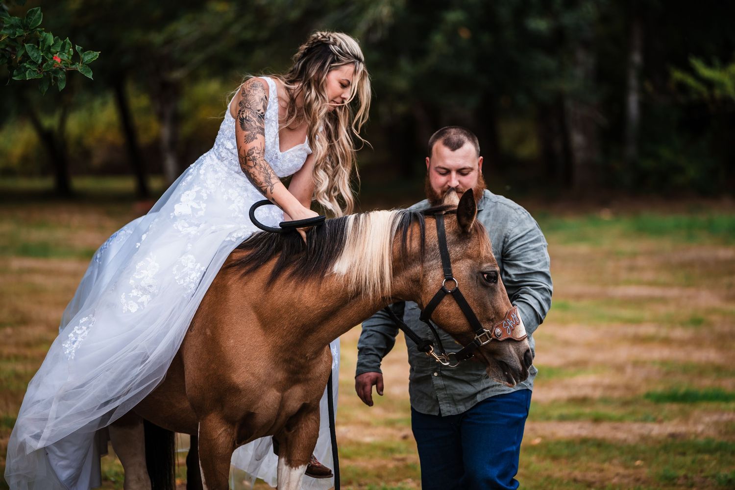 A romantic couple poses with a brown horse during an outdoor photo session in a rustic field setting.