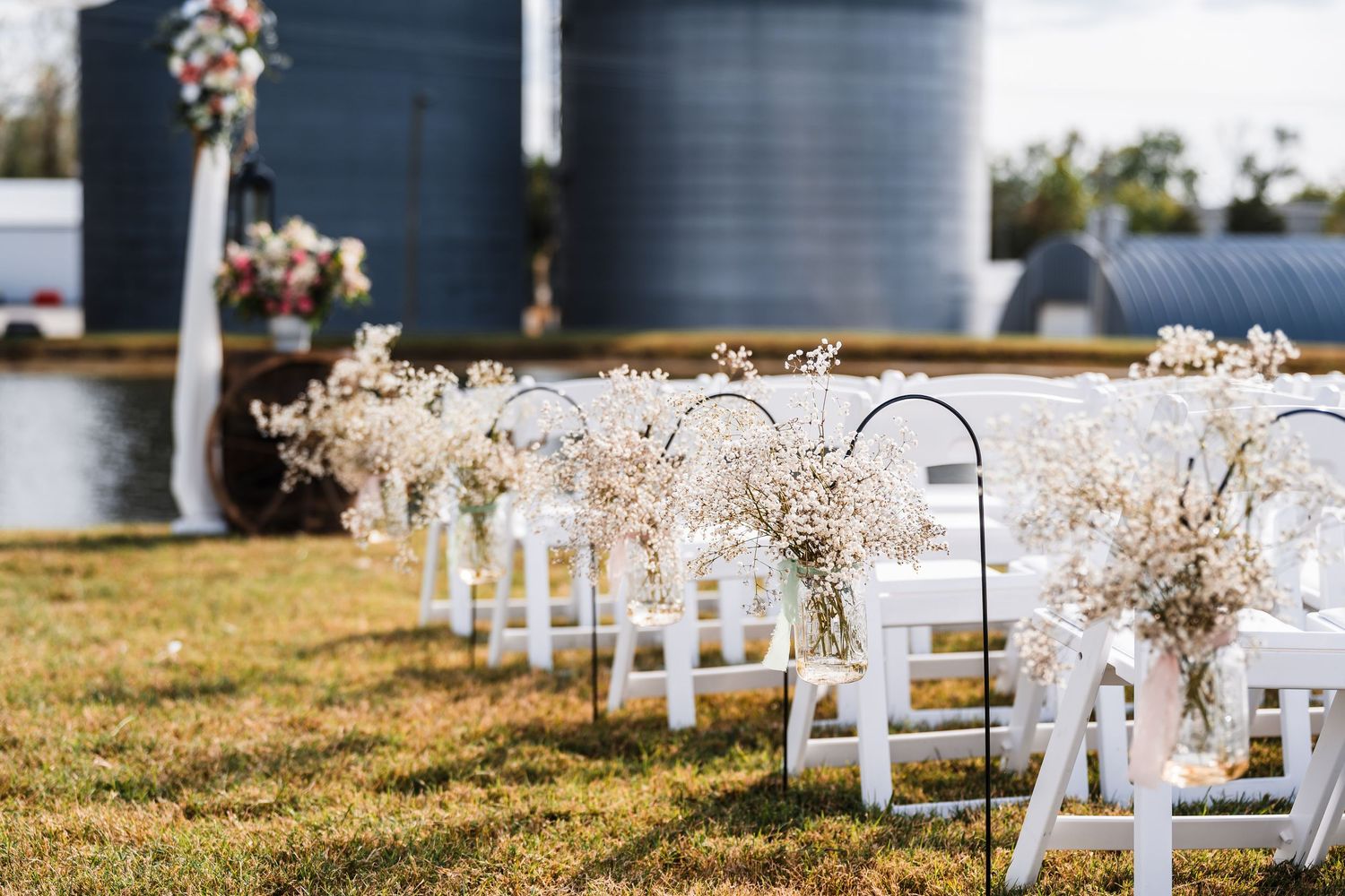 White wooden chairs line up in rows for an outdoor wedding ceremony with autumn leaves scattered on the grass.