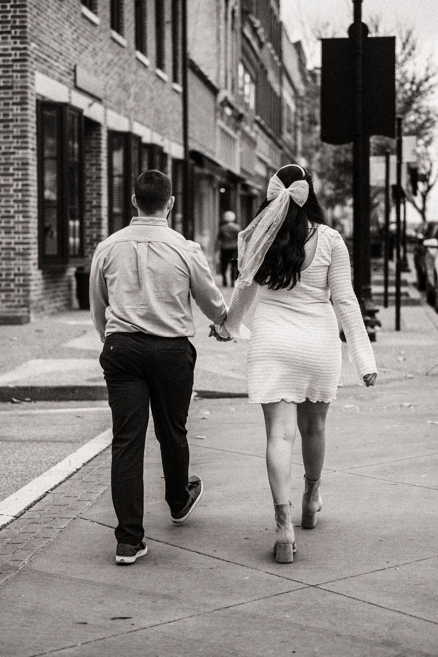 Back view of couple walking hand in hand down city sidewalk in black and white.