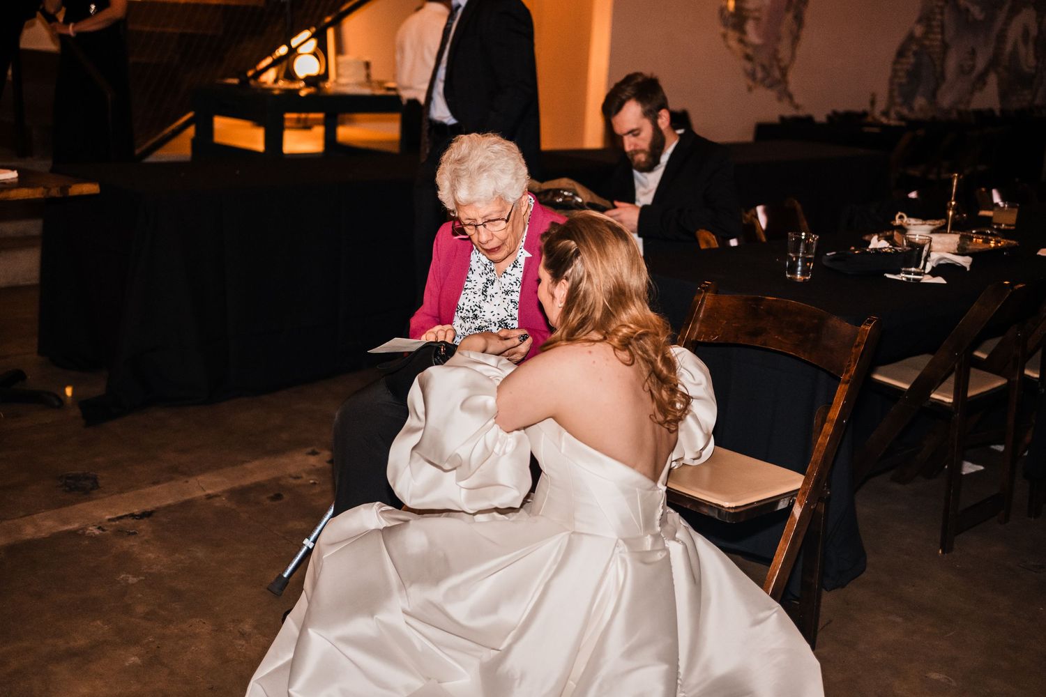 A bride in a white gown kneels down during an intimate moment at the wedding reception.
