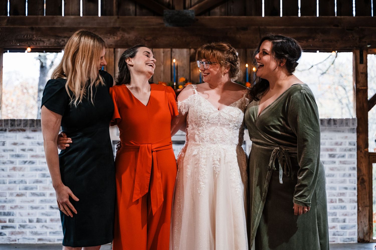 Wedding party in colorful dresses sharing a candid moment together at rustic venue.